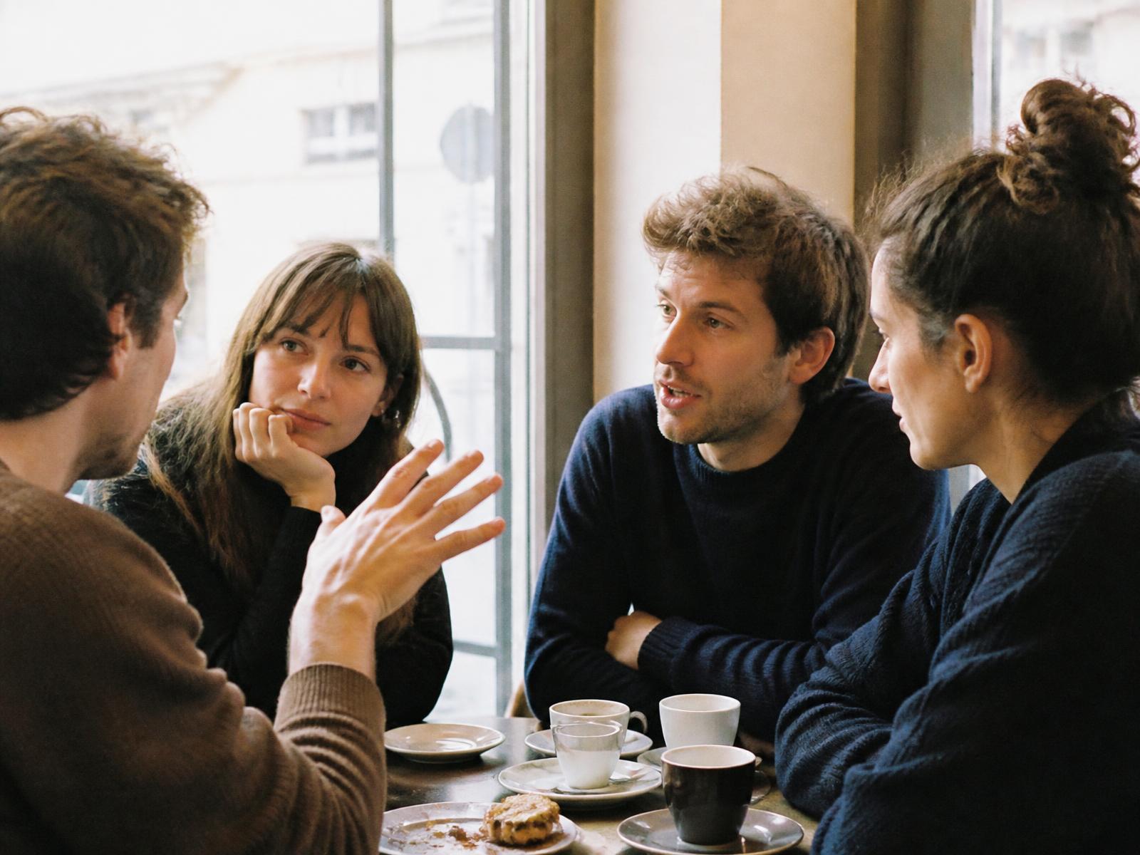 Four adults leaning in over coffee at a café table by a window in daylight